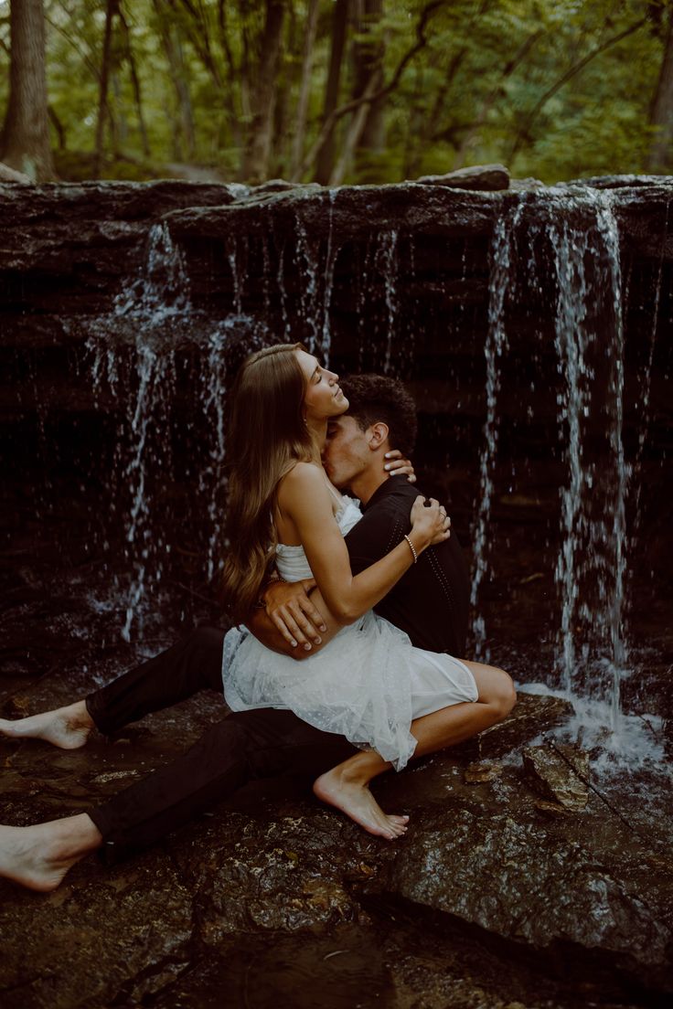 a man and woman sitting on top of a rock next to a waterfall