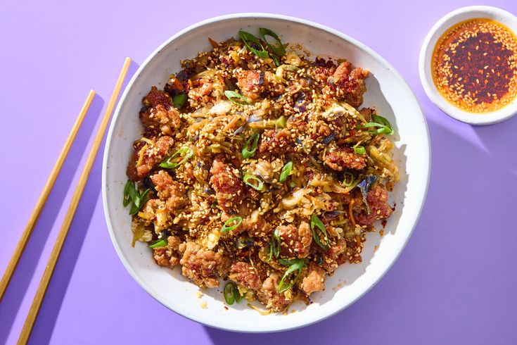 a white bowl filled with food next to chopsticks on a purple tablecloth