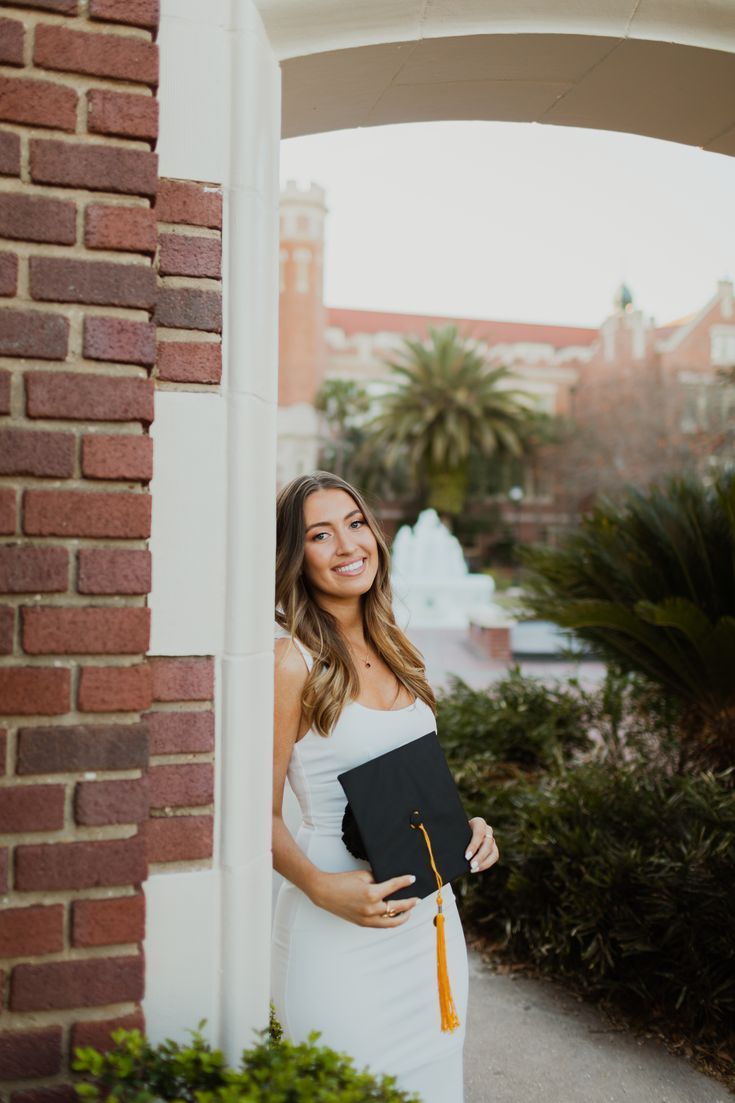 a woman in a white dress is holding a black book and smiling at the camera