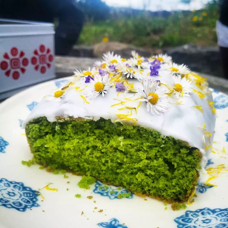 a piece of green cake with white frosting and flowers on it sitting on a plate