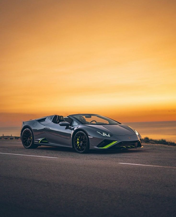 a grey and green sports car driving down the road near the ocean at sunset or dawn