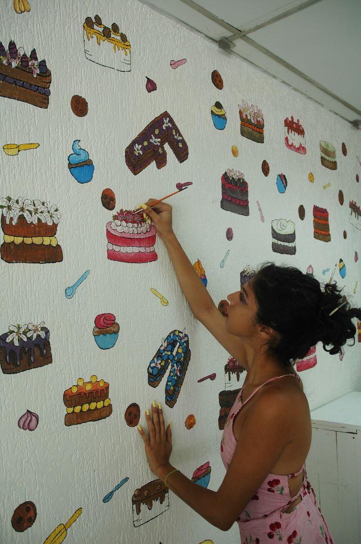 a woman writing on a wall covered in cakes