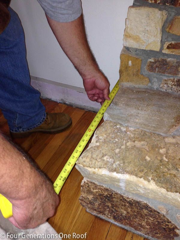 a man measuring the width of a brick wall with a tape measure on wood flooring