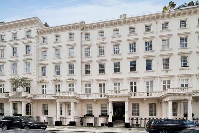 a large white building with many windows and balconies on the top floor, along with cars parked in front of it