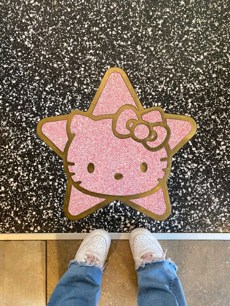 a person standing in front of a hello kitty sticker on the ground with their feet up