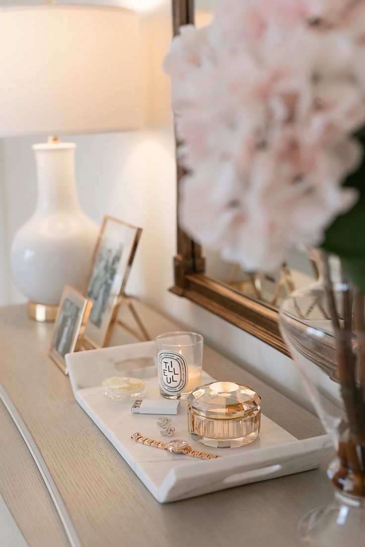 a white tray topped with jewelry next to a vase filled with flowers and a mirror