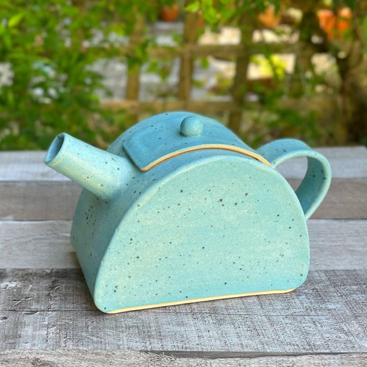 a ceramic teapot sitting on top of a wooden table next to trees and bushes