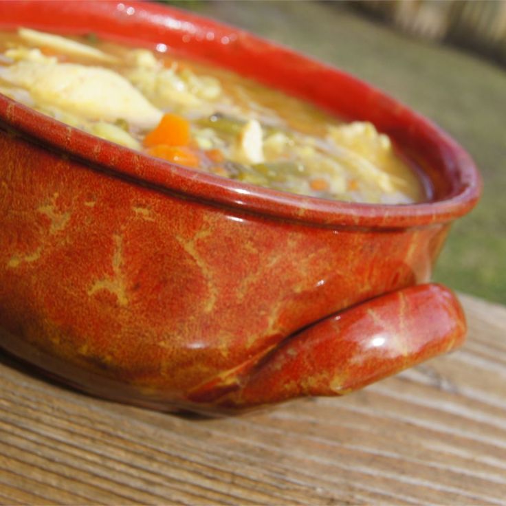 a red bowl filled with soup sitting on top of a wooden table