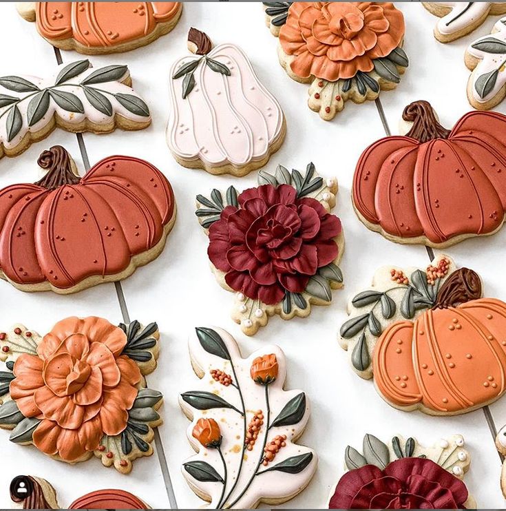 many decorated cookies are arranged on a white surface with flowers and pumpkins in the background