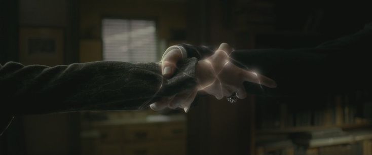 two hands reaching out towards each other in a dark room with bookshelves behind them