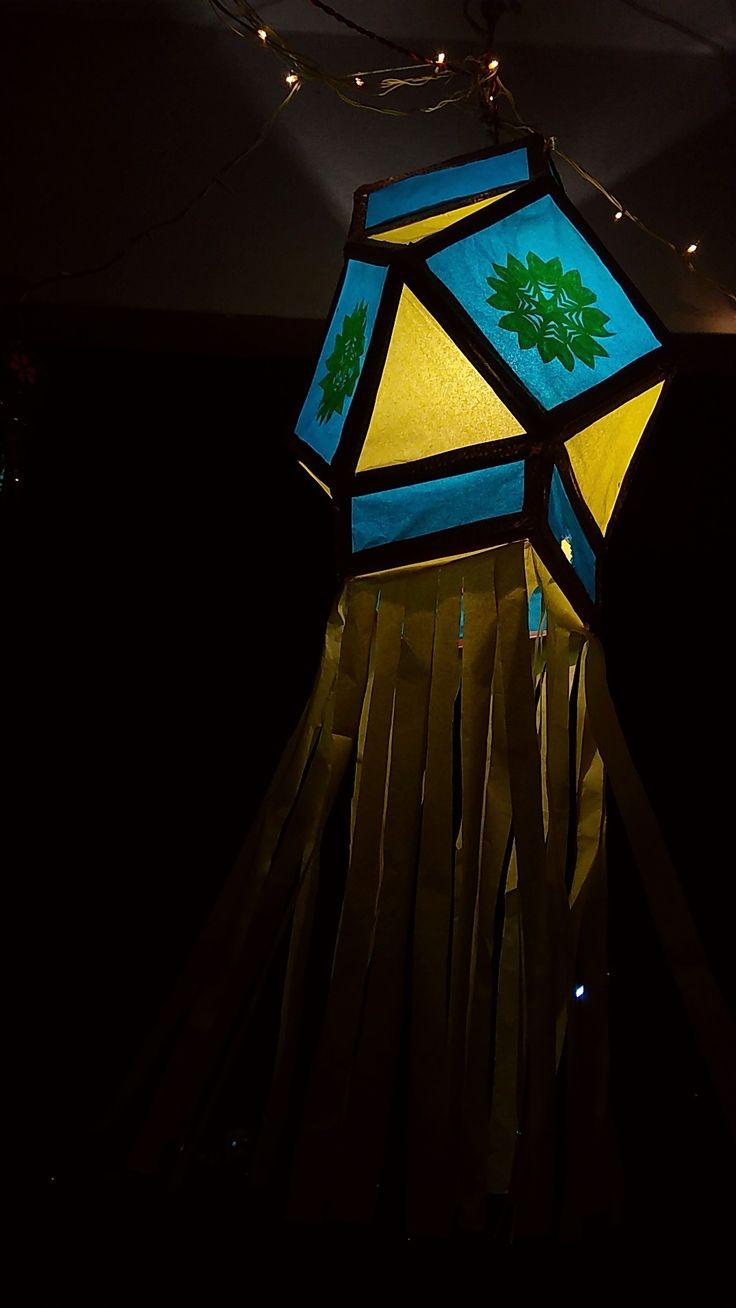 a blue and yellow lamp hanging from the ceiling in a dark room with string lights