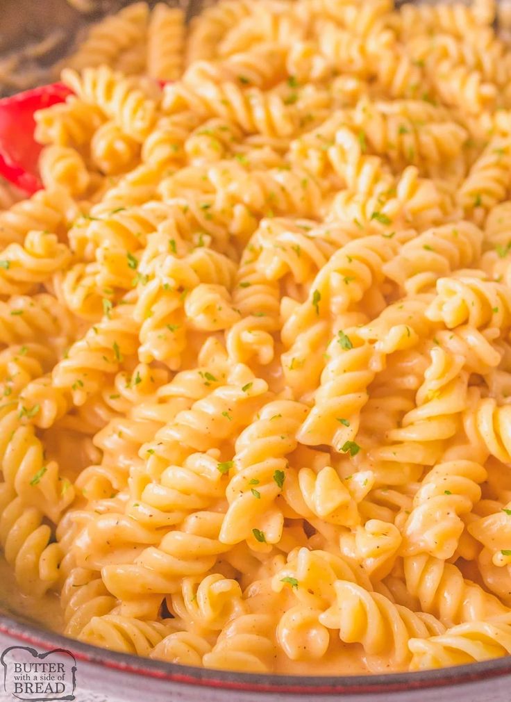 a bowl filled with macaroni and cheese sitting on top of a table next to a red spoon