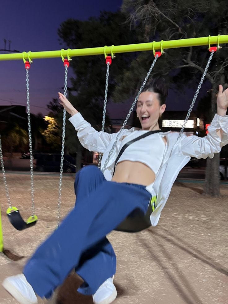 a woman is sitting on a swing at the park