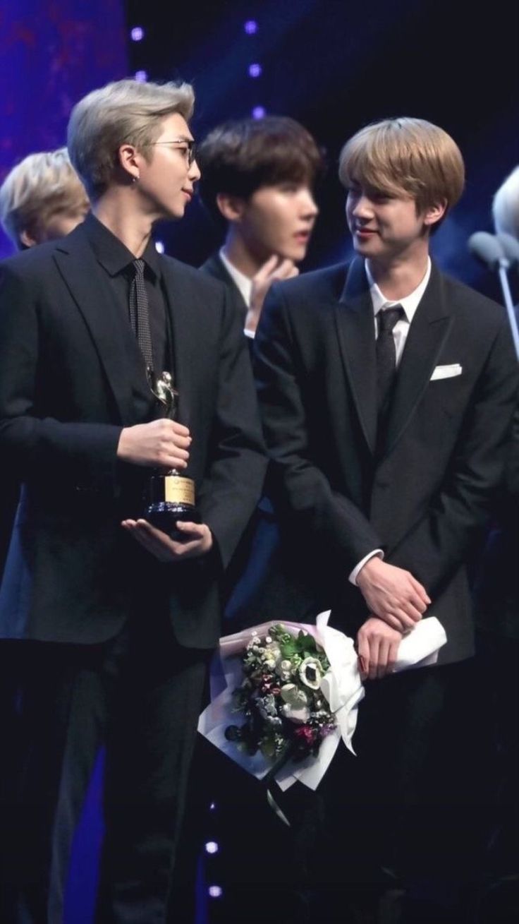 two men in suits are standing next to each other and one is holding a bouquet