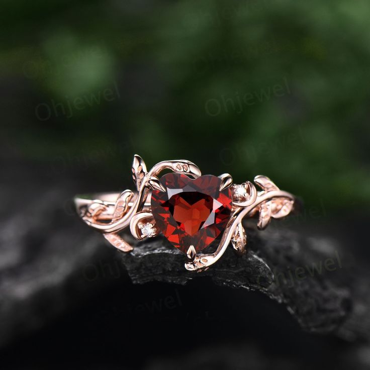 a close up view of a ring with a red stone in the center and leaves on it