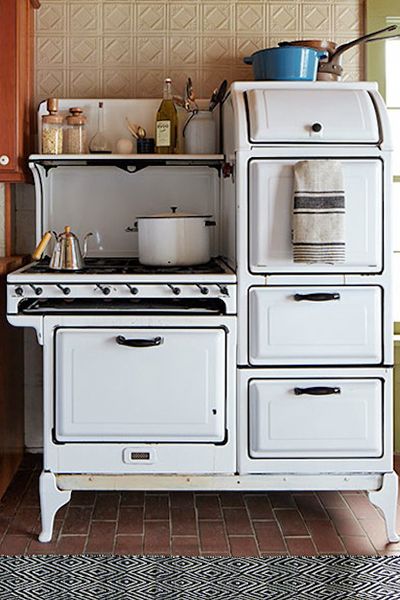 an old fashioned stove in a kitchen with brown tile flooring and white cabinets on the wall