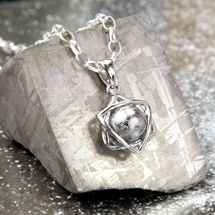 This Meteorite Orb and Star Necklace gives you a chance to carry a little slice of space with you wherever you go. For the person who has everything this unique pendant will highlight your individual style with a piece of natural history round your neck. Consisting of a free spinning orb of meteorite caged in a stylish star shaped silver pendant this makes a beautiful piece of jewellery and an a talking point all in one!. If you've ever yearned to own something from out of this world, here's your chance. Over 100,000 years ago, a handful of these mysterious Muonionalusta meteorites impacted earth. Searches for the impact crater from the original shower have been in vain; the site where these specimens are found is in a remote area of northern Sweden, it is presumed they were carried there Reflective Pool, Meteorite Jewelry, Meteorite Pendant, Crystal Formations, Extra Terrestrial, Climber Earrings, Knot Earrings, Magical Forest, Unique Pendant