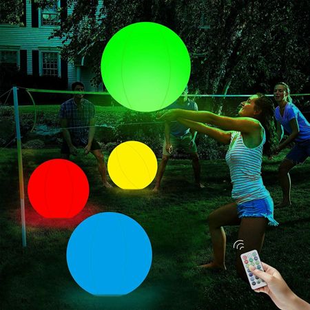 several people are playing with glowing balls in the yard at night, and one person is holding a cell phone