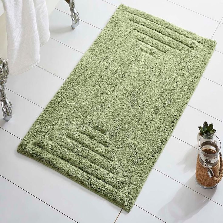 a green rug on the floor next to a potted plant in a white bathroom