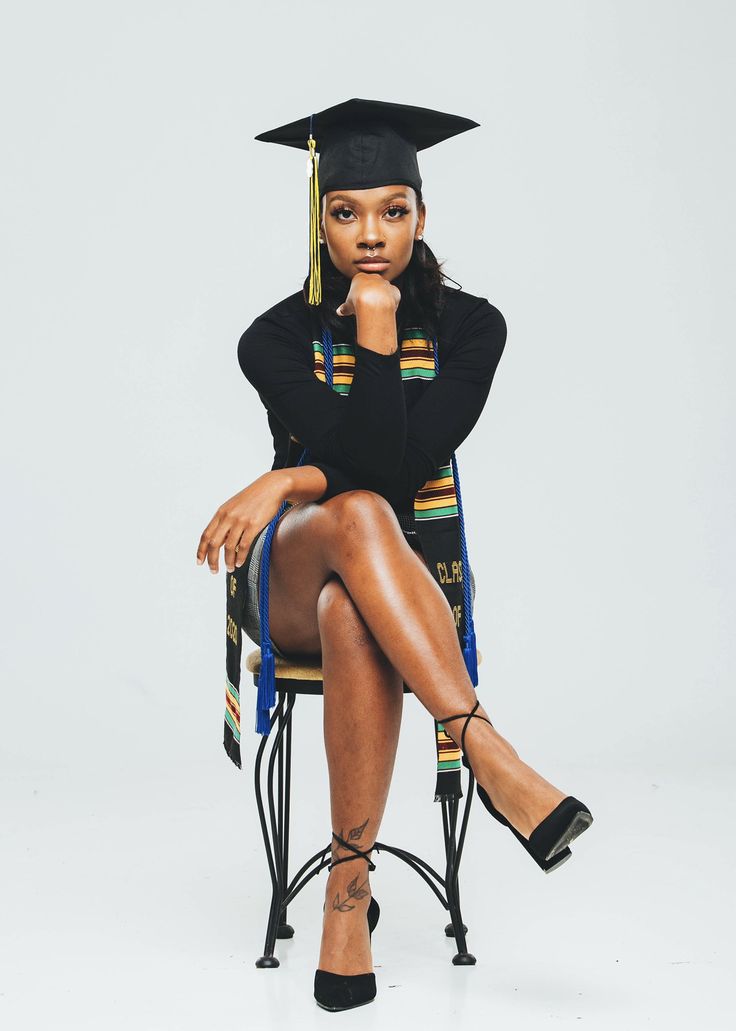 a woman sitting on top of a chair wearing a graduation cap and gown with her legs crossed