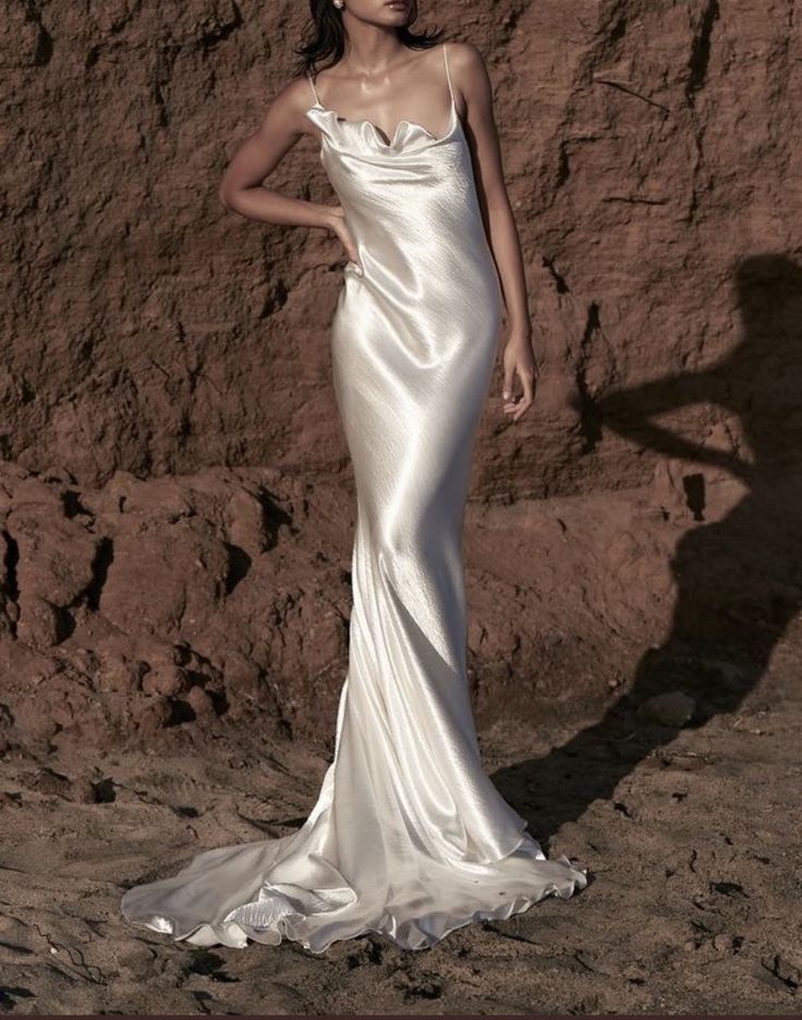 a woman in a long white dress standing next to a rocky cliff with her shadow on the ground