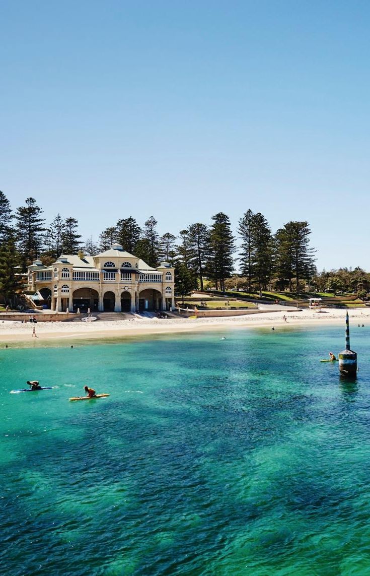 people are swimming in the ocean near a large house with trees on top of it