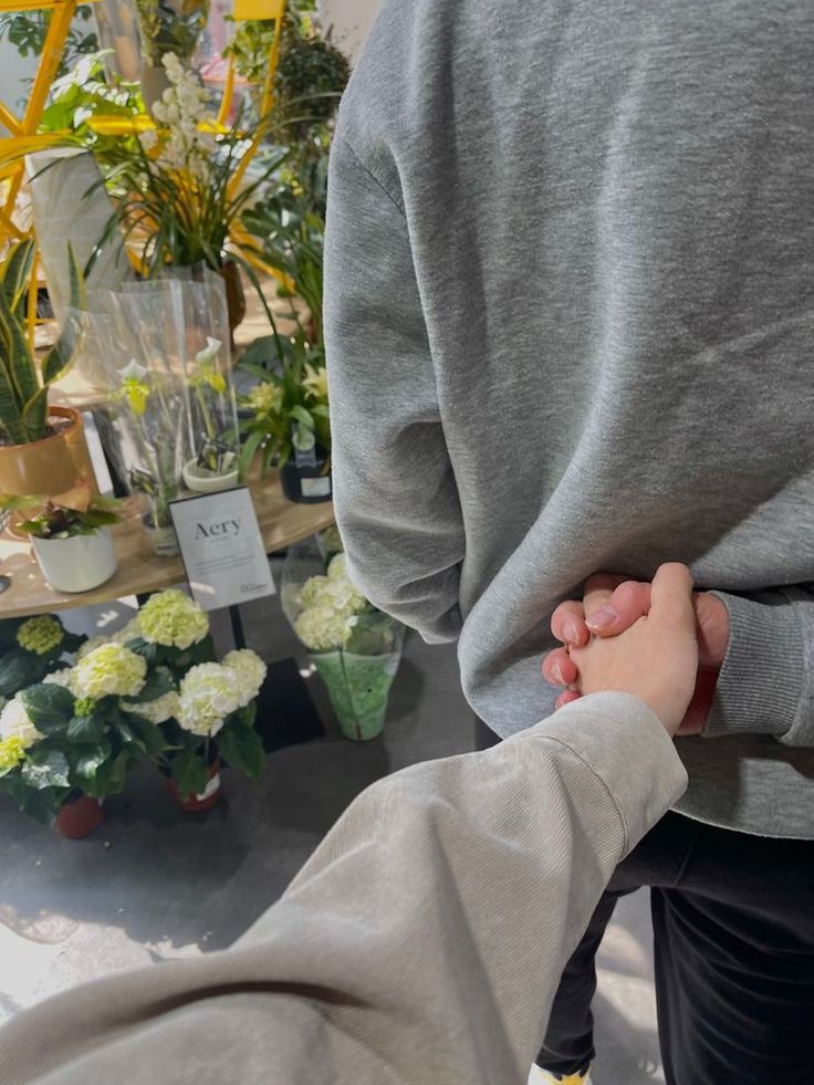 two people are holding hands in front of some potted plants at a flower shop