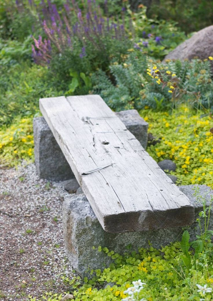 a wooden bench sitting on top of a lush green field next to flowers and rocks