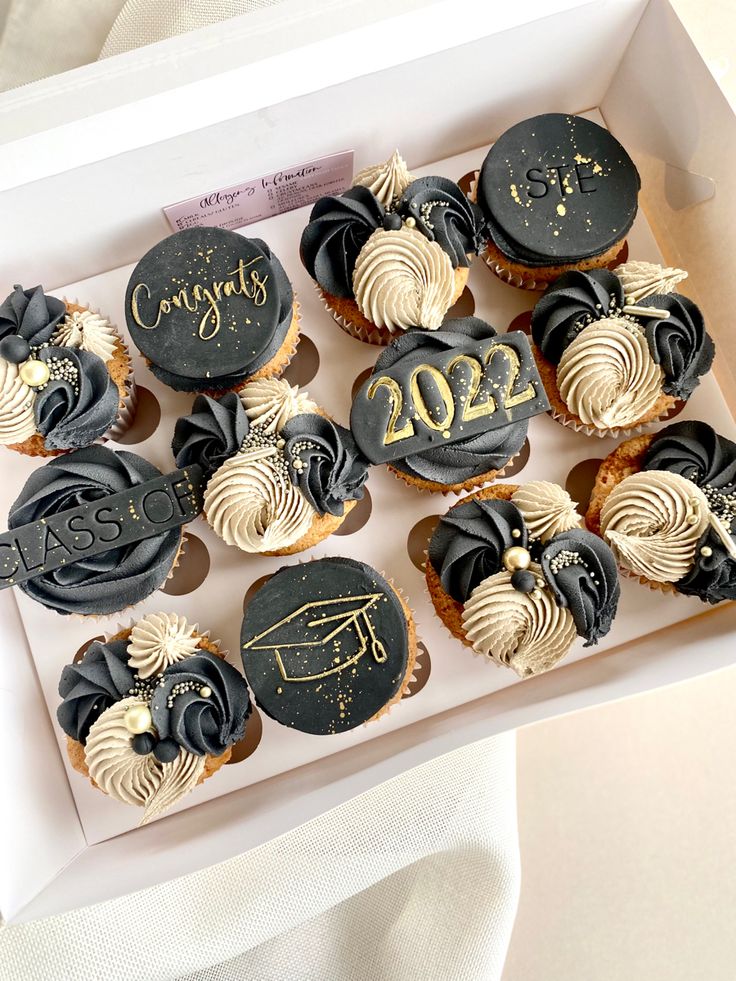 a box filled with cupcakes covered in black and gold frosting next to a napkin