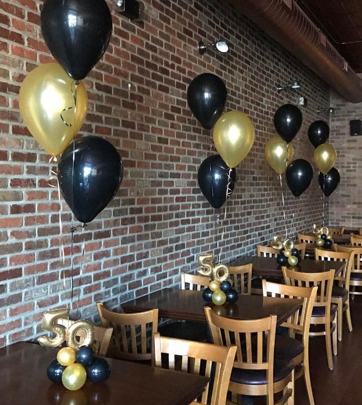 black and gold balloons are hanging from the brick wall in this dining room at a restaurant