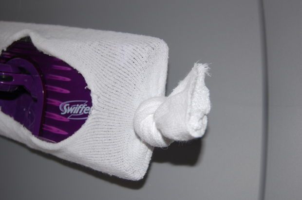 a close up of a toothbrush holder on a gray wall with white cloth and purple swiffer