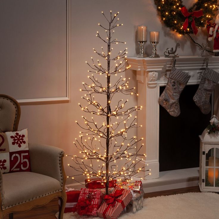 a small christmas tree with lights and presents in front of a fireplace decorated for the holiday season