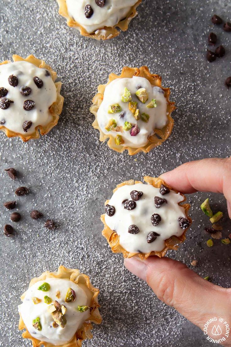 a hand is picking up some cookies with white icing and chocolate chips