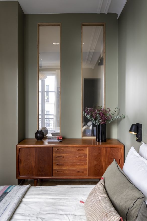 a bed room with a neatly made bed and two large mirrors on the wall above it