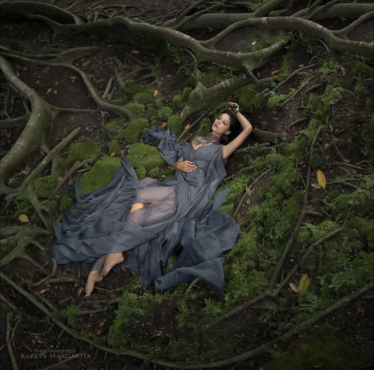 a woman laying on the ground surrounded by mossy trees and branches with her arms behind her head