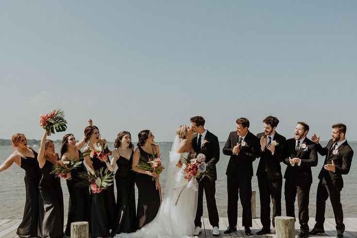 a group of people standing next to each other on a pier near the ocean with flowers in their hands