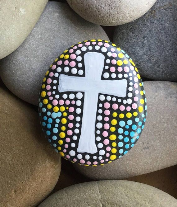 a painted rock with a white cross on it and dots around the edge, sitting on top of some rocks