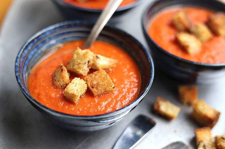 two bowls of tomato soup with croutons on the side