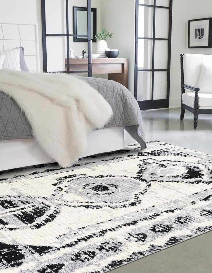 a white and black bedroom with a large rug on the floor next to a bed