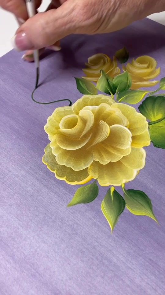 a person is painting flowers on a piece of purple paper with yellow and green leaves