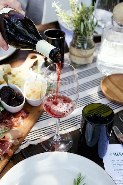 a person pouring red wine into a glass at a table with food and utensils