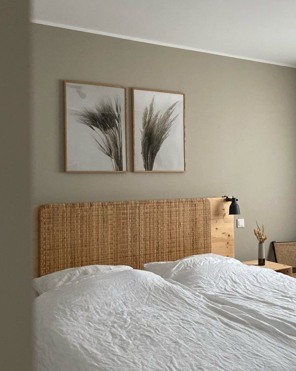 two framed pictures hang on the wall above a bed with white linens and wicker headboard