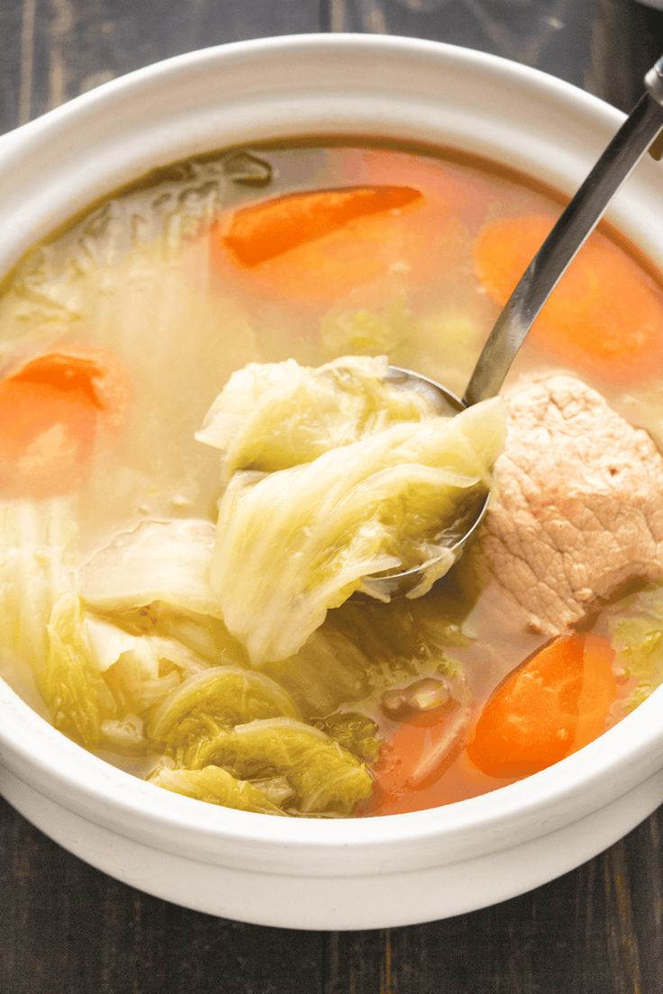 a white bowl filled with cabbage and carrots next to a spoon on top of a wooden table