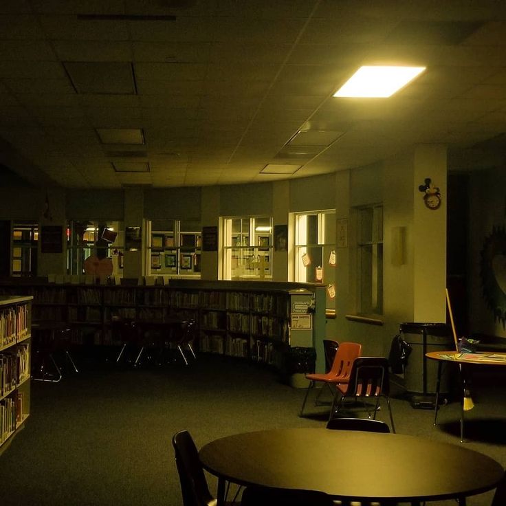 an empty library with many bookshelves and tables in the dark, at night