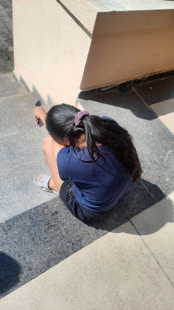 a woman sitting on the ground writing on a wall next to a cement block with her legs crossed