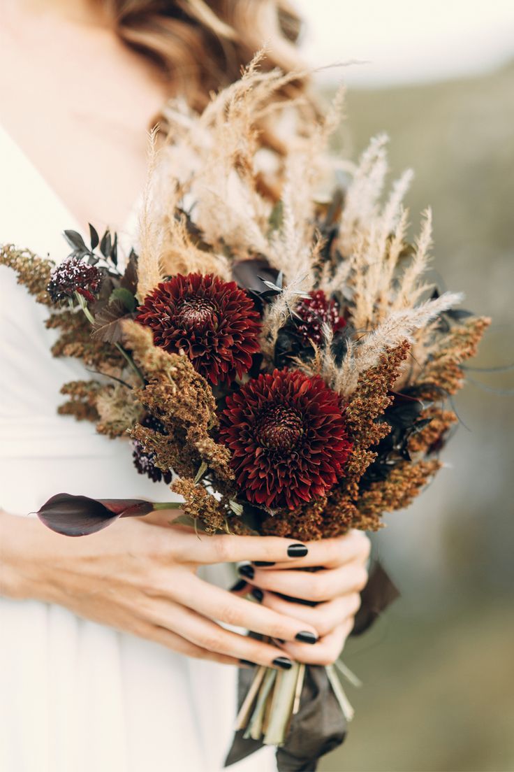 a woman holding a bouquet of dried flowers in her hands and wearing a white dress