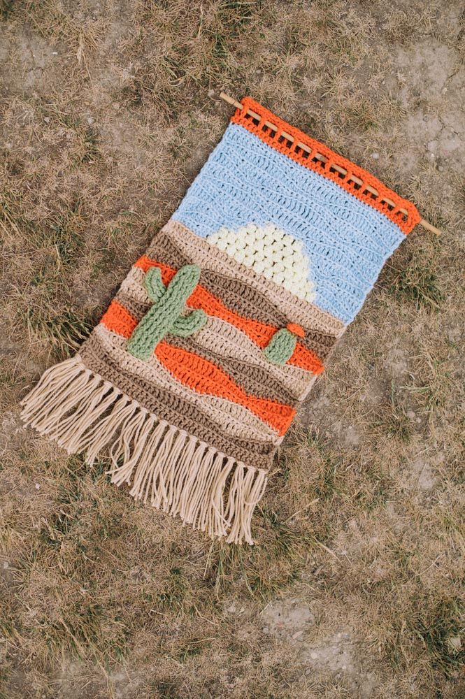 a crocheted blanket laying on the ground with a cactus design and tassels