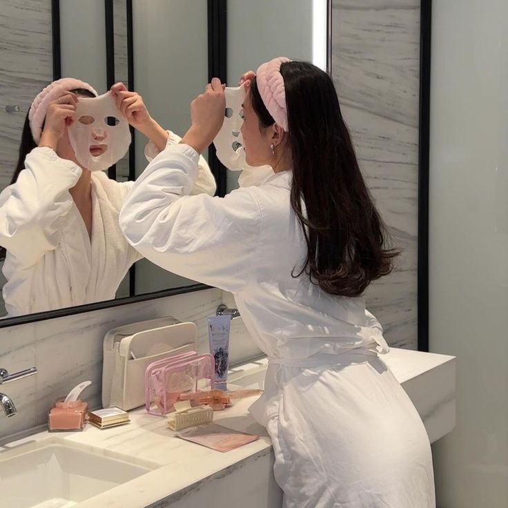 a woman in a bathrobe brushing her hair while looking at herself in the mirror