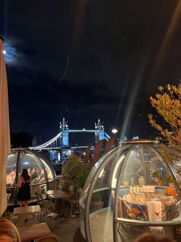 people are sitting at tables in an open air restaurant with the tower bridge in the background