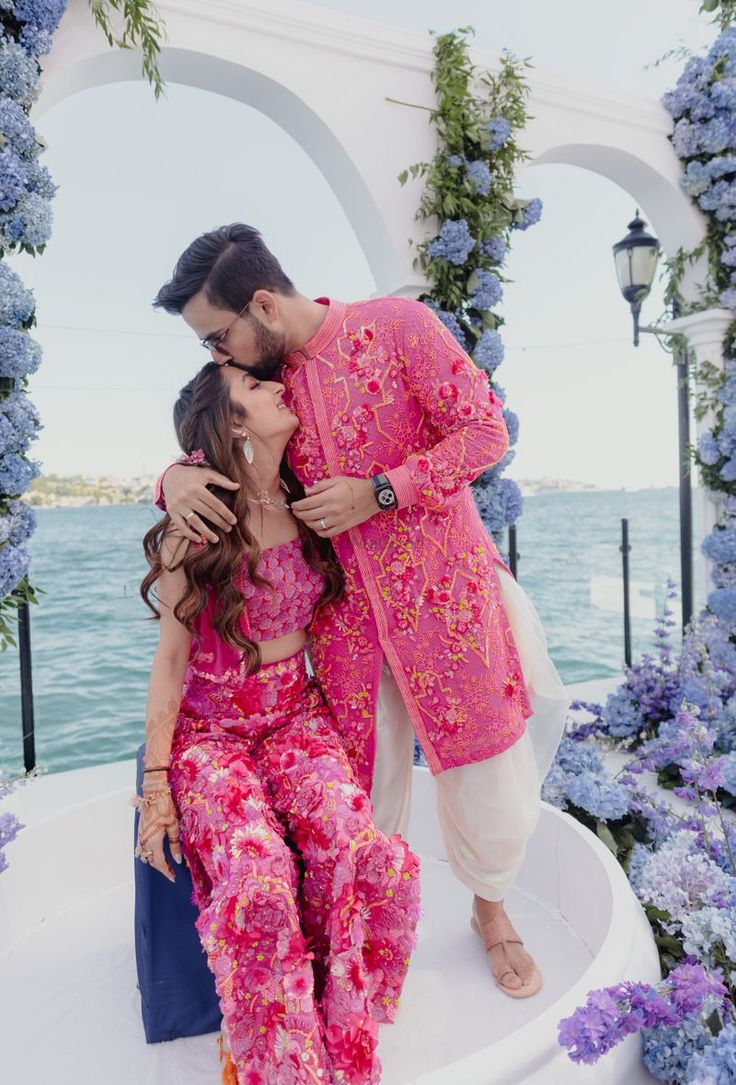 a man and woman are kissing in front of some flowers on the water's edge